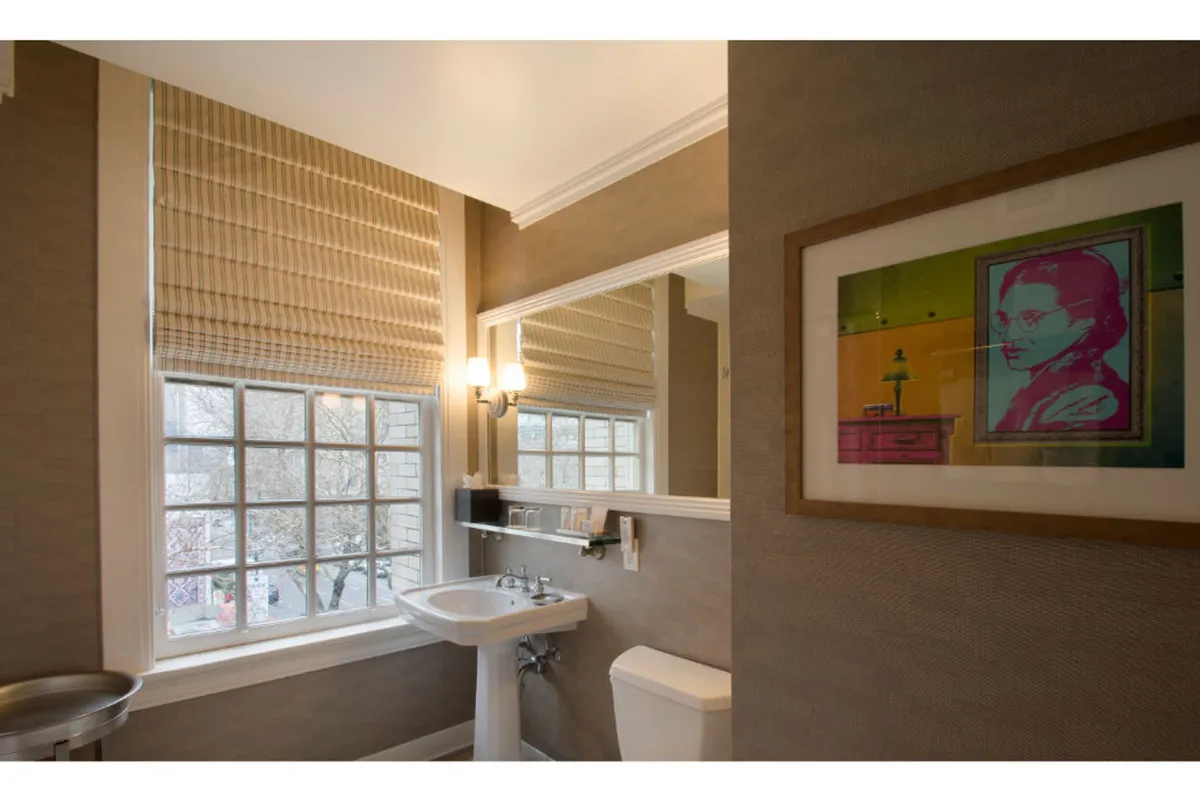 This image highlights a modern bathroom vanity with a broad sink, large mirror, and stylish artwork. Sunlight streams through the window, enhancing the feeling of warmth and cleanliness. The space is arranged for personal grooming and relaxation, emphasizing the expansive counter and soft lighting.