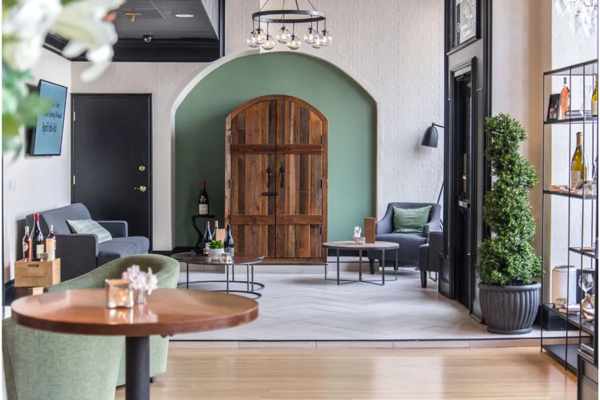 A stylish seating area featuring a cozy arrangement with a green accent wall, wooden door, and a display shelf, suggesting a welcoming and modern atmosphere suited for both relaxation and productivity.