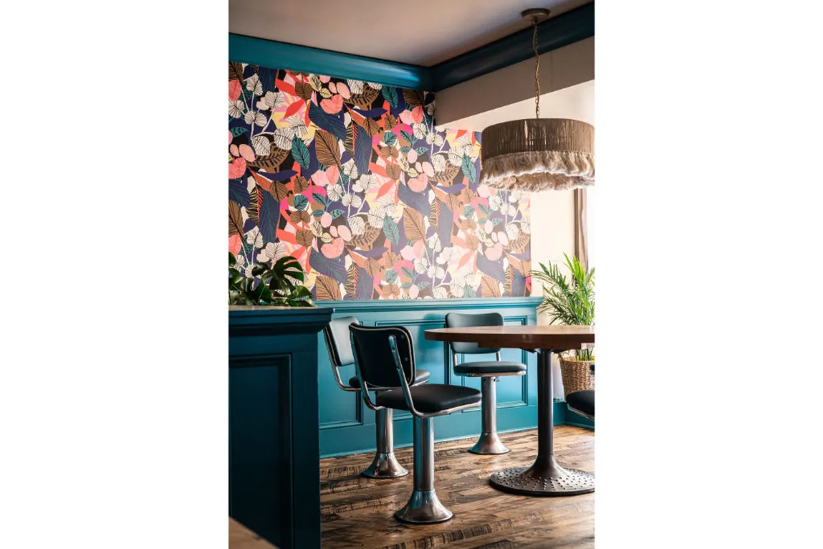A vibrant space highlighted by colorful floral wallpaper, a modern dining table, stylish chairs, and a hanging light fixture, exuding a cheerful yet upscale vibe ideal for casual relaxation or enjoying a coffee break.