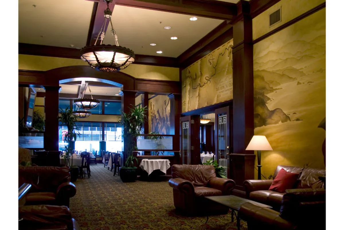 An opulent seating area with ornate chandeliers, richly decorated wall murals, and comfortable leather seating surrounded by potted plants. The space feels both glamorous and intimate, ideal for quiet conversation or special occasions.