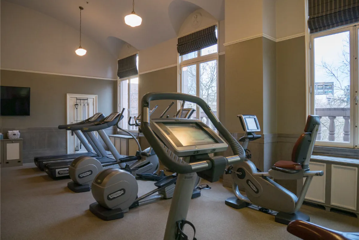 A bright, motivational fitness center featuring treadmills, elliptical machines, and large windows that let in ample natural light. Wall-mounted TVs provide entertainment, and the space is set for both solo workouts and group fitness sessions.